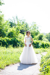 Happy bride in a long white wedding dress and veil in a green park on nature. Wedding image of a young girl, women's makeup and hairstyle. Marriage concept