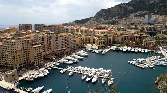 Harbor for boats in Monte Carlo surrounded by residential houses, hotels. Boats at european pier shot from above, private vehicles and houses on background of mountains