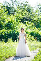 Happy bride in a long white wedding dress and veil in a green park on nature. Wedding image of a young girl, women's makeup and hairstyle. Marriage concept