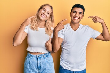 Young interracial couple wearing casual white tshirt smiling cheerful showing and pointing with fingers teeth and mouth. dental health concept.