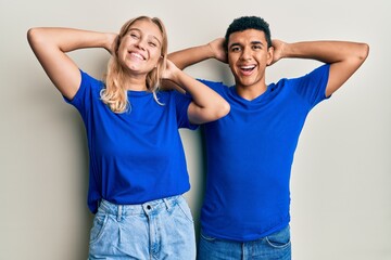 Young interracial couple wearing casual clothes relaxing and stretching, arms and hands behind head and neck smiling happy