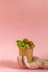 Fried bean balls, falafel, in a paper Cup. Holds the hand in a protective glove. Healthy food delivery concept