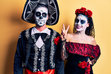 Young couple wearing mexican day of the dead costume over yellow showing and pointing up with...