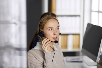 Friendly businesswoman talking by headset in office. Call center and diverse people group in business
