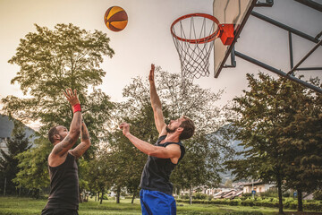 Two friends jump at basketball.