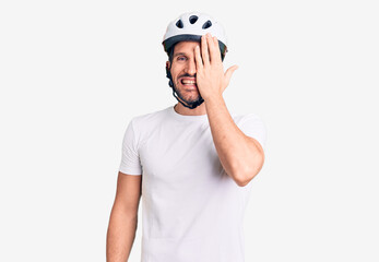 Young handsome man wearing bike helmet covering one eye with hand, confident smile on face and surprise emotion.