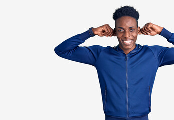 Young african american man wearing sportswear smiling pulling ears with fingers, funny gesture. audition problem