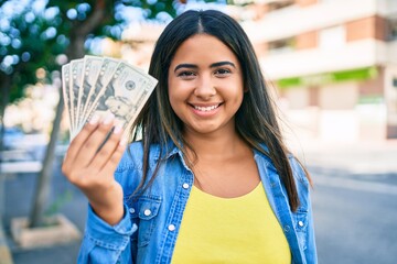 Young latin woman smiling happy holding usa dollars banknotes at city.