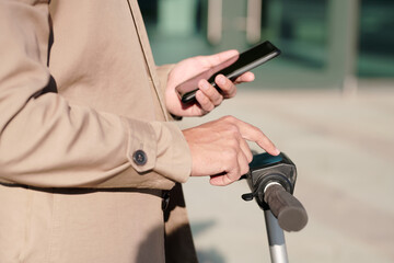 Hand of modern businessman in beige trenchcoat scrolling in smartphone