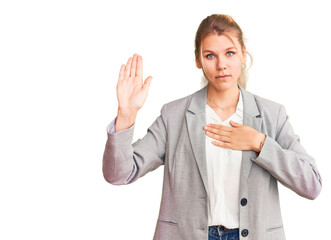Young beautiful blonde woman wearing elegant jacket swearing with hand on chest and open palm,...