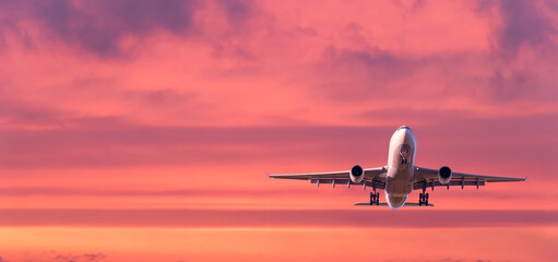 Airplane is flying in colorful sky at sunset. Landscape with white passenger airplane, purple sky...