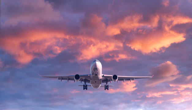 Airplane is flying in colorful sky at sunset. Landscape with white passenger airplane, purple sky with pink clouds. Aircraft is landing. Business trip. Commercial plane. Travel. Aerial view. Concept © den-belitsky