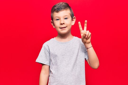 Cute blond kid wearing casual clothes smiling with happy face winking at the camera doing victory sign. number two.