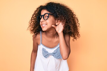African american child with curly hair wearing casual clothes and glasses smiling with hand over...