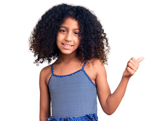 African american child with curly hair wearing swimwear smiling with happy face looking and pointing to the side with thumb up.