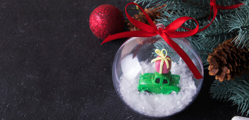 Transparent christmas ball with a toy car and a gift in the snow on a dark background