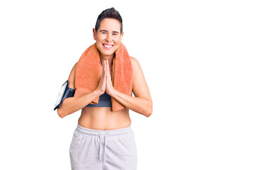 Young woman with short hair wearing sportswear and towel using smartphone praying with hands together asking for forgiveness smiling confident.