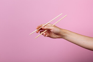 Hands holding chopsticks. Isolated on pink background, the place for caption and text