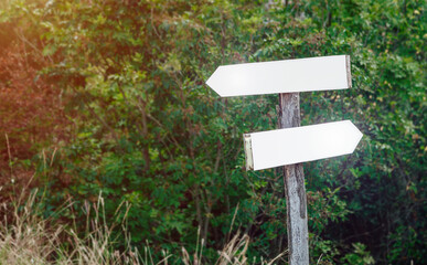 Blank track pointers or guidepost against green nature background. Directional arrow signs on wooden pole in the forest.