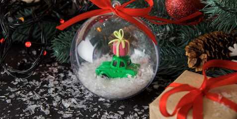 Transparent christmas ball with a toy car and a gift in the snow on a dark background