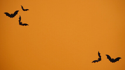 Halloween holiday concept. Black paper bats on bright orange background, top view, flat lay,copy spaes.Celebration of the dead