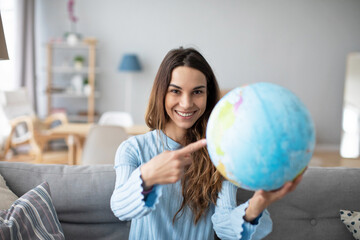 Woman dreaming about travel, pointing with index finger at globe. Planning vacation.