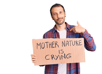 Young handsome man holding mother nature is crying protest cardboard banner pointing finger to one self smiling happy and proud