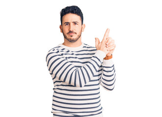 Naklejka premium Young hispanic man wearing casual clothes holding symbolic gun with hand gesture, playing killing shooting weapons, angry face