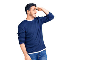 Young hispanic man wearing casual clothes very happy and smiling looking far away with hand over head. searching concept.