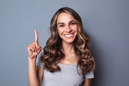 Happy smiling caucasian woman points up while posing over gray wall. Female portrait.