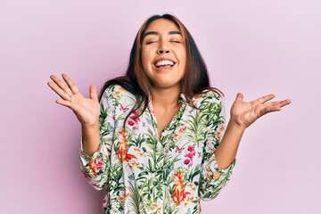 Young latin woman wearing casual clothes celebrating mad and crazy for success with arms raised and...
