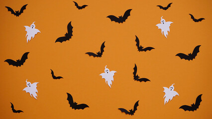 Fototapeta na wymiar Halloween decoration concept - seamless pattern with black paper bats and ghosts on orange background, flat lay.Celebration of the dead