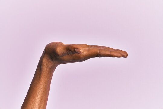 Arm and hand of black middle age woman over pink isolated background with flat palm presenting product, offer and giving gesture, blank copy space