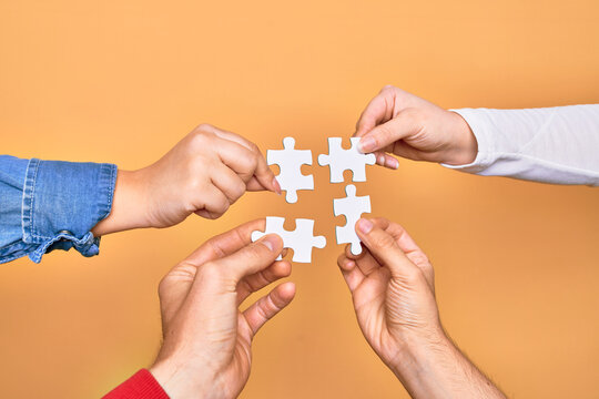 Hands of caucasian young people connecting pieces of puzzle over isolated yellow background