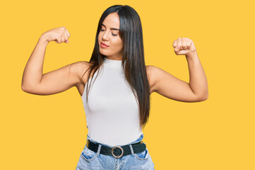 Young beautiful hispanic girl wearing casual clothes showing arms muscles smiling proud. fitness concept.