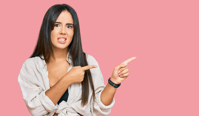 Young beautiful hispanic girl wearing casual clothes pointing aside worried and nervous with both hands, concerned and surprised expression