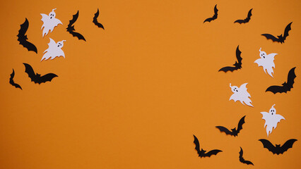 Halloween holiday concept. Black paper bats and ghosts on bright orange background, top view, flat lay,copy spaes.Celebration of the dead