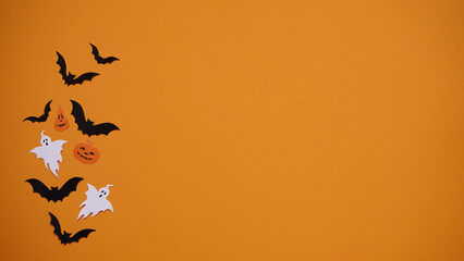 Halloween holiday concept. Black paper bats and ghosts on bright orange background, top view, flat lay,copy spaes.Celebration of the dead