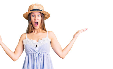 Obraz na płótnie Canvas Beautiful brunette young woman wearing summer hat celebrating victory with happy smile and winner expression with raised hands