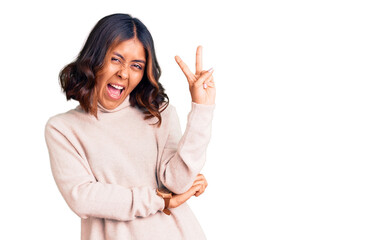 Young beautiful mixed race woman wearing winter turtleneck sweater smiling with happy face winking at the camera doing victory sign with fingers. number two.