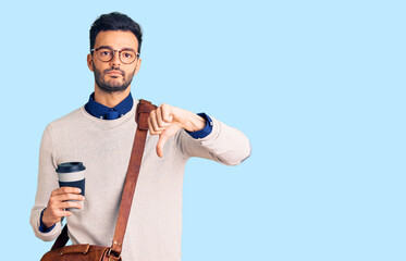 Young handsome hispanic man wearing leather bag and drinking take away coffee with angry face,...