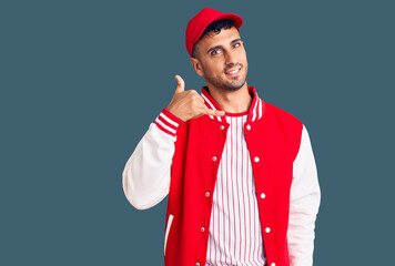 Young hispanic man wearing baseball uniform smiling doing phone gesture with hand and fingers like talking on the telephone. communicating concepts.