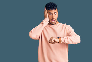 Young hispanic man wearing casual clothes looking at the watch time worried, afraid of getting late