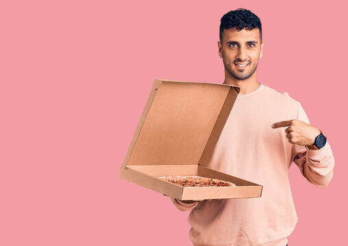 Young hispanic man holding delivery pizza box pointing finger to one self smiling happy and proud