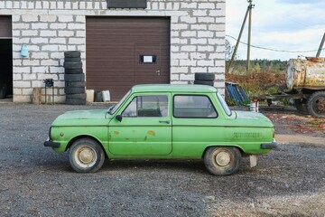 Old abandoned rusted light green colored soviet retro car near the auto repair shop ready for tuning.