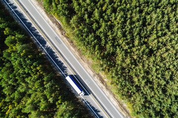The truck is driving along an asphalt highway. Looking like a highway, the road runs through the forest. The forest is located on both sides of the road