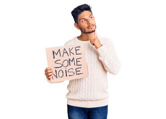 Handsome latin american young man holding make some noise banner serious face thinking about...