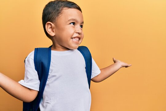 Adorable latin toddler smiling happy wearing student backpack over isolated yellow background.