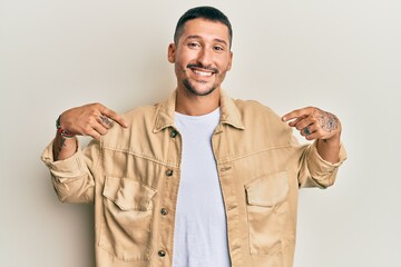 Handsome man with tattoos wearing casual brown denim jacket looking confident with smile on face,...