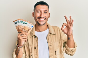 Handsome man with tattoos holding 50 euro banknotes doing ok sign with fingers, smiling friendly gesturing excellent symbol - obrazy, fototapety, plakaty